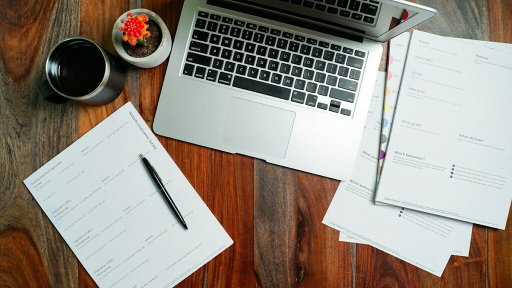 Ordinateur portable ouvert sur un bureau en bois, entouré de feuilles de travail et d'une tasse