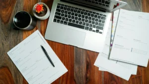 Ordinateur portable ouvert sur un bureau en bois, entouré de feuilles de travail et d'une tasse